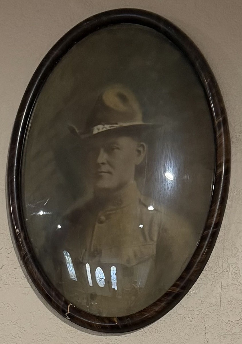 An oval portrait of Thompson Hanes in First World War uniform and campaign hat, in a dark wood frame under convex glass, hanging on a wall.